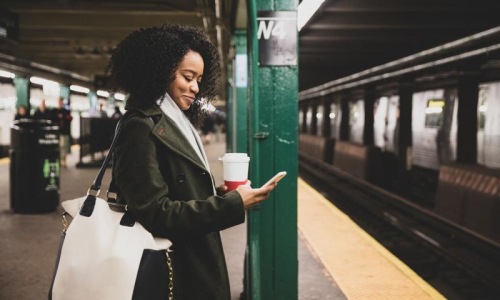 Find your perfect fit at Mackie Flats woman with a cup of coffee texts on subway station platform